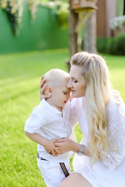 Giovane bella madre seduta con bambino sull'erba in cortile. e baciare il bambino — Foto Stock