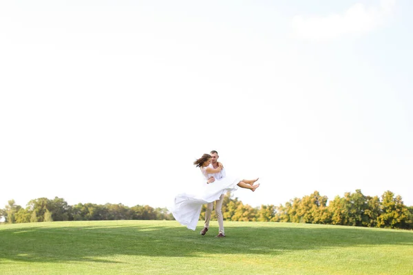 Noivo feliz segurando noiva na grama no fundo do céu branco . — Fotografia de Stock