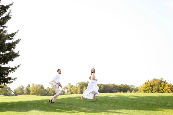 Pan młody i panna młoda biegają i bawią się na trawie. — Zdjęcie stockowe