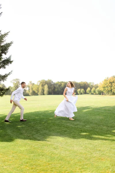 Noivo e caucasiano noiva correndo e jogando na grama . — Fotografia de Stock