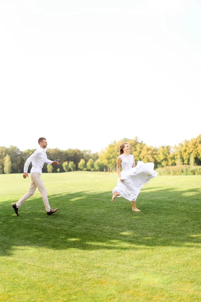 Bruidegom en bruid in witte jurk lopen en spelen op gras. — Stockfoto