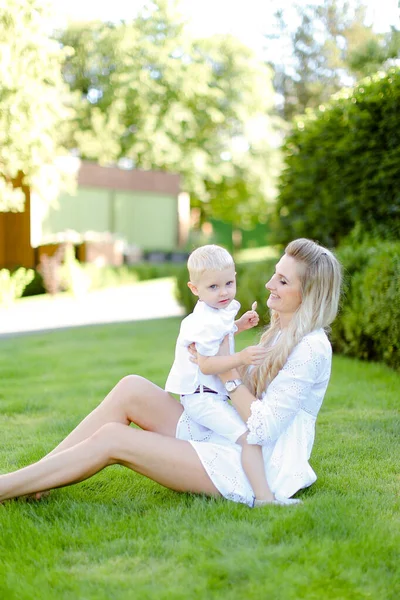 Giovane bella madre seduta con piccolo bambino sull'erba in cortile . — Foto Stock