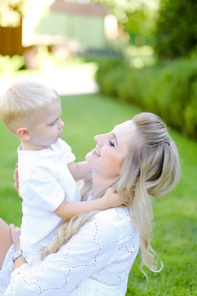 Giovane madre sorridente seduta e pagante con piccolo bambino sull'erba in cortile . — Foto Stock