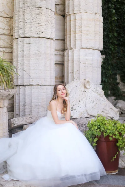 Λευκή νύφη κάθεται κοντά σε αρχαίους κίονες και φοράει λευκό φόρεμα. — Φωτογραφία Αρχείου