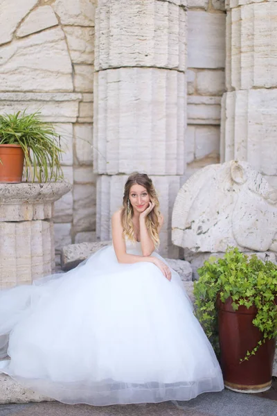 Λευκή όμορφη νύφη κάθεται κοντά σε αρχαίους κίονες και φοράει λευκό φόρεμα. — Φωτογραφία Αρχείου