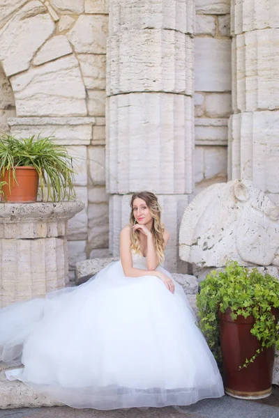 Καυκάσια ωραία νύφη κάθεται κοντά σε αρχαίες στήλες και φοράει λευκό φόρεμα. — Φωτογραφία Αρχείου