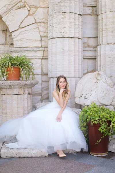 Caucasian charming bride sitting near ancient columns and wearing white dress. — Φωτογραφία Αρχείου