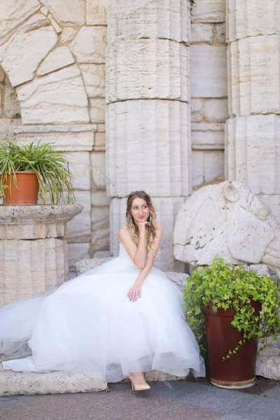 Noiva europeia caucasiana sentado perto de colunas antigas e vestindo vestido branco . — Fotografia de Stock