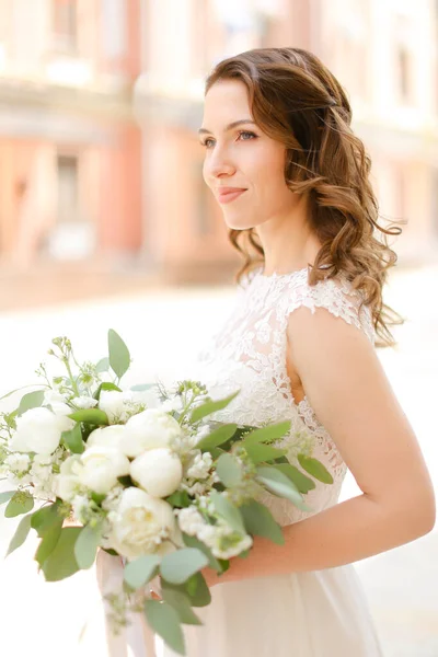 Ευτυχισμένη καυκάσια νύφη κρατώντας μπουκέτο από λουλούδια και φορώντας λευκό φόρεμα. — Φωτογραφία Αρχείου