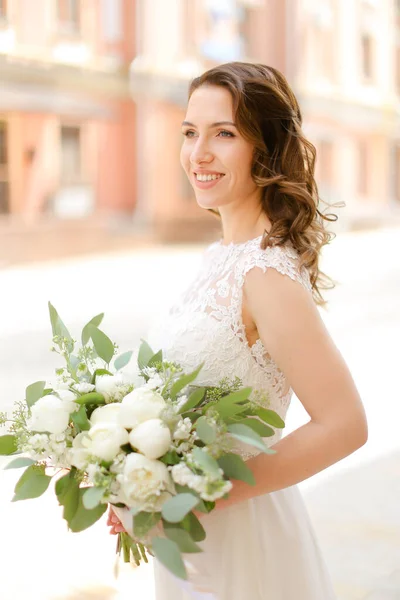 Happy european pengantin menjaga karangan bunga dan mengenakan gaun putih . — Stok Foto