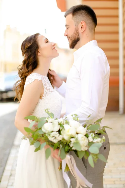 Glad vacker brudgum kramar fästmö hålla blommor och bär vit klänning. — Stockfoto