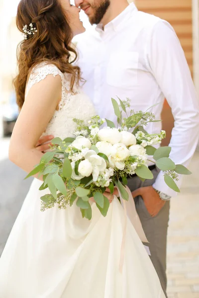 Happy Kaukasia pengantin laki-laki memeluk tunangan menjaga bunga dan mengenakan gaun putih . — Stok Foto