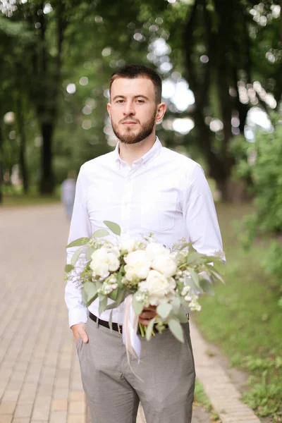 Kaukasischer schöner Bräutigam wartet auf Braut mit Blumenstrauß. — Stockfoto