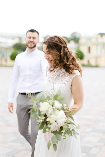 Vit brud promenader med vacker brudgum bukett blommor i staden. — Stockfoto