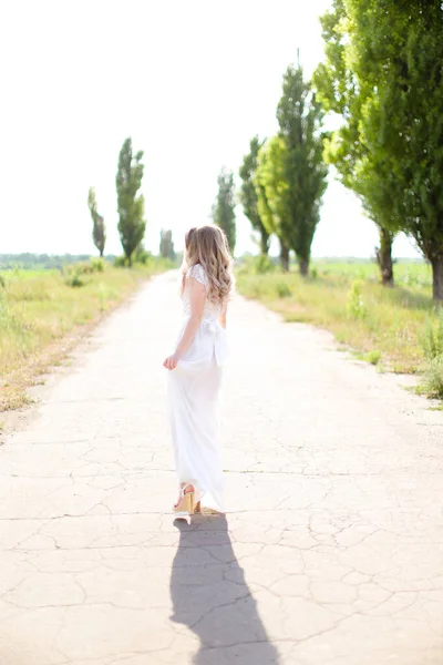 Vue arrière de la jeune femme européenne portant une robe blanche marchant sur la route . — Photo