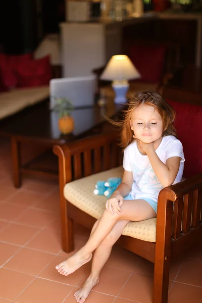 Little european female model sitting with toy in wooden chair.