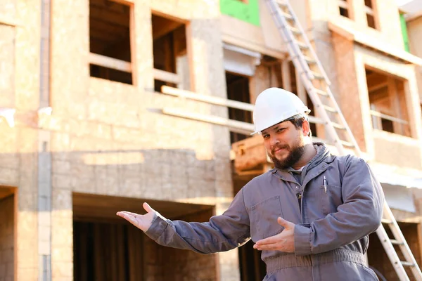 Retrato de construtor caucasiano mostrando edifício pronto e vestindo hardhat . — Fotografia de Stock