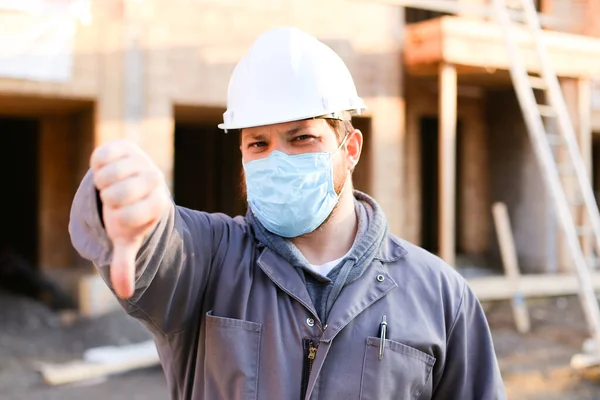 Foreman usando máscara e chapéu duro no local de construção mostrando polegares para baixo . — Fotografia de Stock