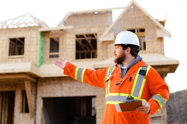 Turuncu elbiseli ustabaşı inşaat alanında defter tutuyor..