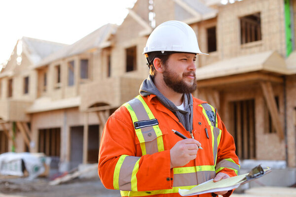 Caucasian foreman writing in notebook on construction site.