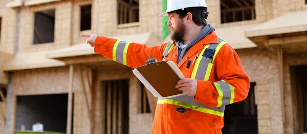 Прапор інженера в помаранчевому робочому одязі, що тримає ноутбук на будівельному майданчику . — стокове фото
