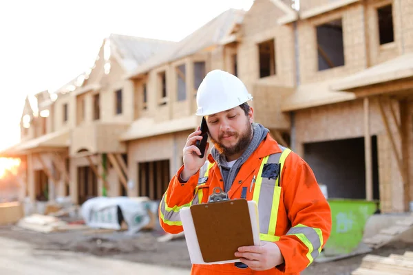 Caucasian foreman talking by smartphone and looking at blueprint. Royalty Free Stock Photos