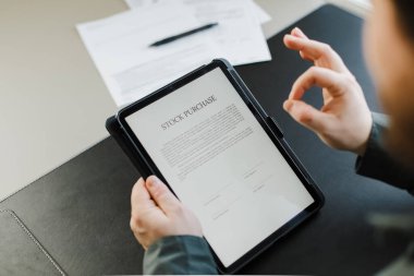 Tablet üzerinde hisse senedi satın alma sözleşmesi okuyan ve iyi niyet gösteren bir adam.