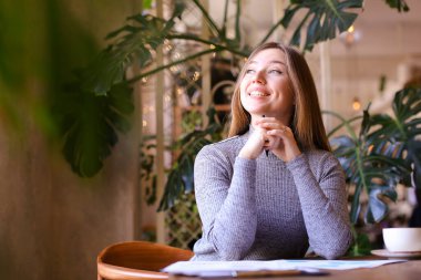 Kafede dometnlerle çalışan genç bir iş kadını, masada fincan..