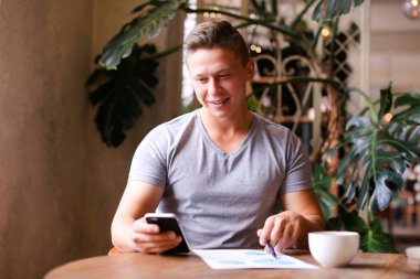 Belgeler ve akıllı telefon kafe ile çalışan genç serbest çalışan bir erkek..