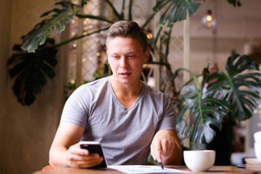 Belgeler ve akıllı telefon kafe ile çalışan kendine güvenen genç işadamı.