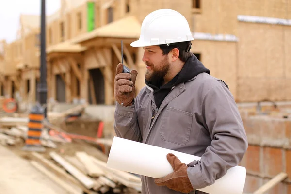 Construtor falando por walkie talkie e segurando plano de desenho no canteiro de obras. — Fotografia de Stock