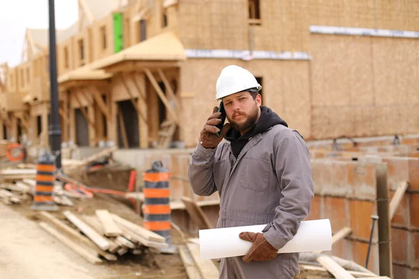 Builder μιλώντας από το smartphone και κρατώντας σχέδιο στο εργοτάξιο. — Φωτογραφία Αρχείου