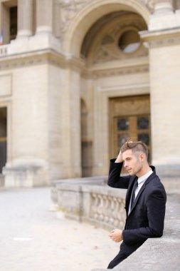 Genç damat binanın yanındaki beton tırabzana yaslanıp bekliyor..