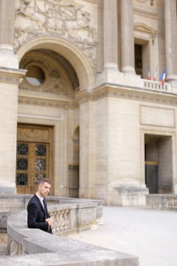 Genç işadamı binanın yanındaki beton tırabzanda bekliyor ve yaslanıyor..