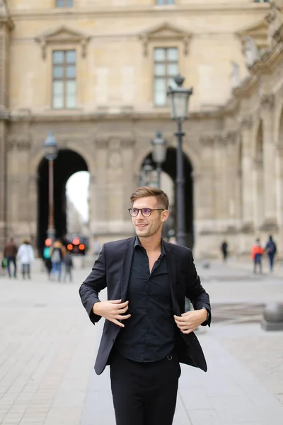 Young man walking in Paris and wearing black suit.