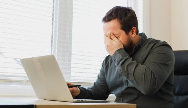 Üzgün işadamı gözlerini kapatıyor ve ofiste dizüstü bilgisayar kullanıyor..