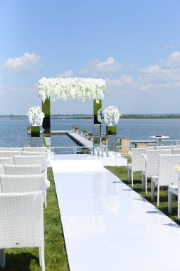 Beyaz muhteşem düğün kemeri ve göl kenarındaki sandalyeler.