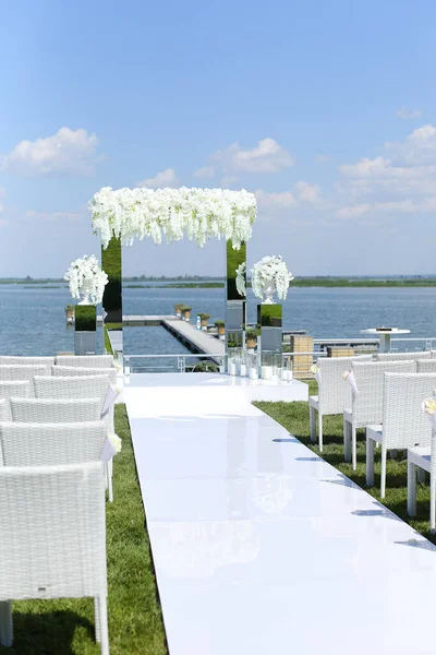Beyaz muhteşem düğün kemeri ve göl kenarındaki sandalyeler.