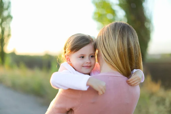 Blonde woman holding female kid and walking on road. — Stock Photo, Image