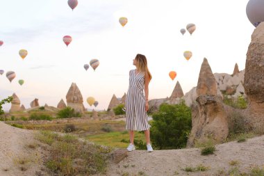 Kapadokya, Türkiye 'de arka planda çok sayıda sıcak hava balonuyla ayakta duran kız.