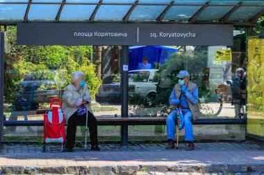 Uzhgorod, Ukrayna - 3 Haziran 2020: Koruyucu maskeli / eldivenli yaşlılar otobüs durağındaki bankta oturmuş sosyal mesafenin kurallarına uyarak konuşuyorlar. COVID-19 Hastalık Koruma Programı.