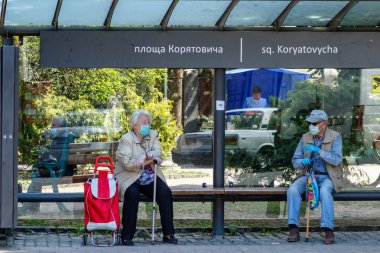 Uzhgorod, Ukrayna - 3 Haziran 2020: Koruyucu maskeli / eldivenli yaşlılar otobüs durağındaki bankta oturmuş sosyal mesafenin kurallarına uyarak konuşuyorlar. COVID-19 Hastalık Koruma Programı.