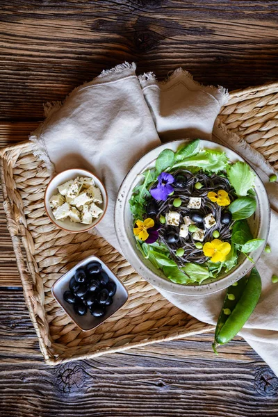 Salată de paste de fasole neagră cu frunze verzi, măsline, mazăre verde, brânză de oaie și flori comestibile — Fotografie, imagine de stoc