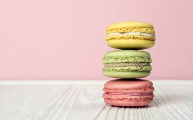 Ahşap masa ve pembe bir arka plan üzerinde yığılmış Fransızca macaroons