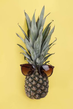 Sarı arka planda güneş gözlüğü takan ananas.