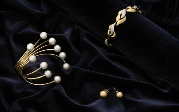 Pulseiras douradas e brincos par em fundo de tecido de veludo azul — Fotografia de Stock