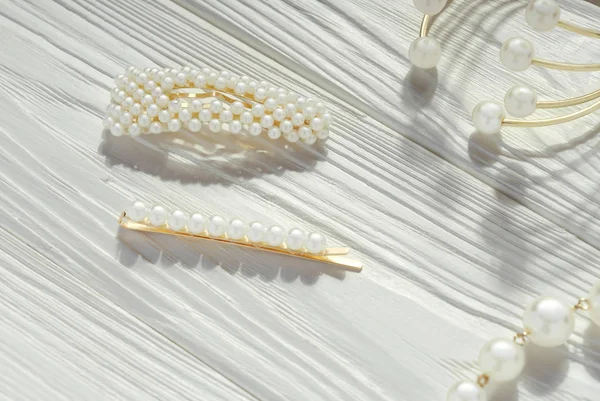 Pinos de cabelo dourados e pérolas e pulseira dourada na mesa de madeira branca — Fotografia de Stock