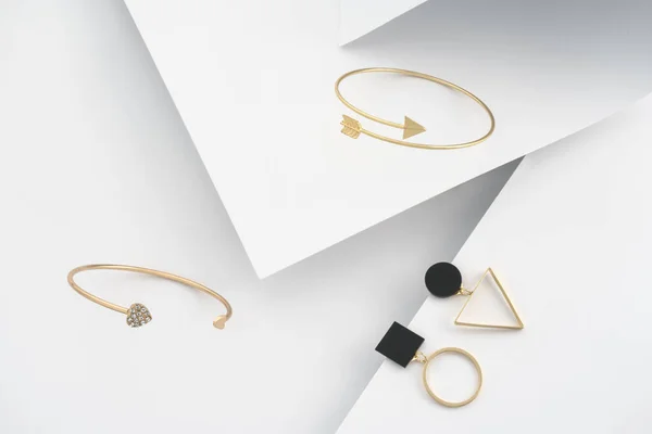 Современный дизайн золотые браслеты и геометрические серьги на белом бумажном фоне — стоковое фото