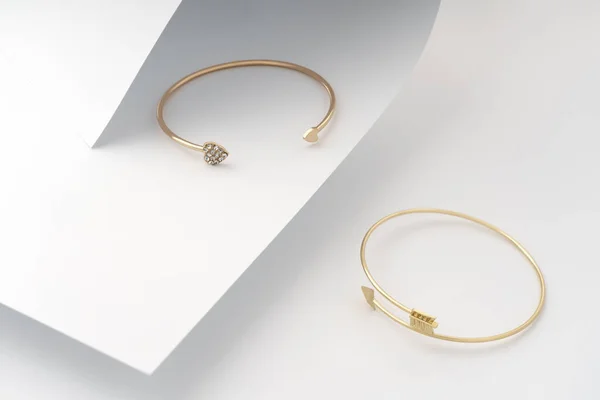 Arrow and heart shape golden bracelets on folded white paper background