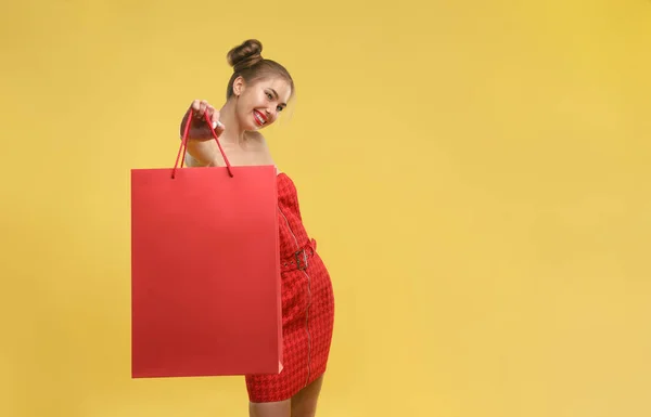 Happy girl in red dress holding red shopping bag isolated on yellow background — Stock Photo, Image